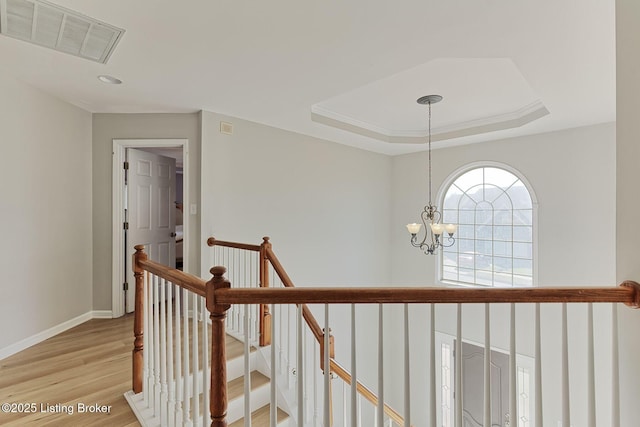 hallway featuring light hardwood / wood-style floors, a raised ceiling, and a chandelier