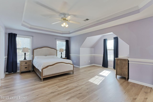 bedroom with a raised ceiling, ornamental molding, multiple windows, and light hardwood / wood-style flooring