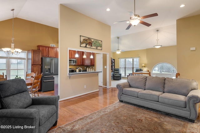 living room featuring ceiling fan with notable chandelier, high vaulted ceiling, and light wood-type flooring