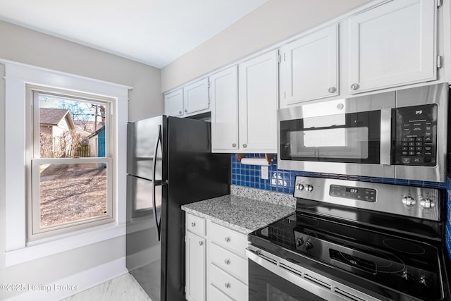 kitchen with stainless steel appliances, white cabinetry, light stone countertops, and backsplash