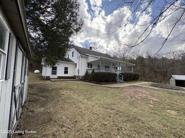 view of side of property featuring a storage unit, covered porch, and a lawn