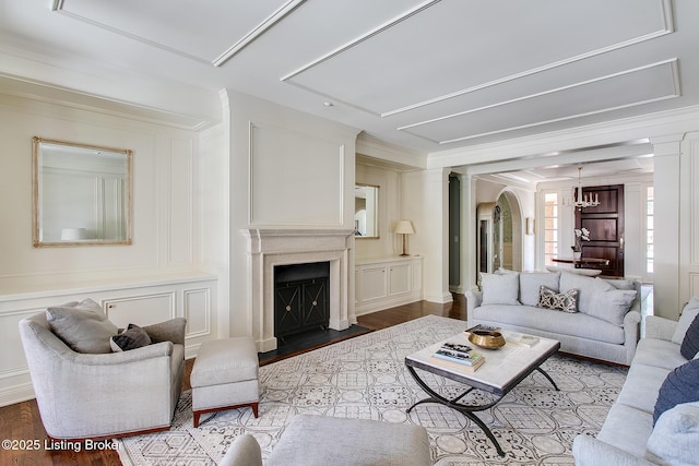 living room featuring a notable chandelier, crown molding, decorative columns, and hardwood / wood-style flooring