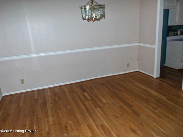 unfurnished dining area featuring a chandelier, baseboards, and wood finished floors