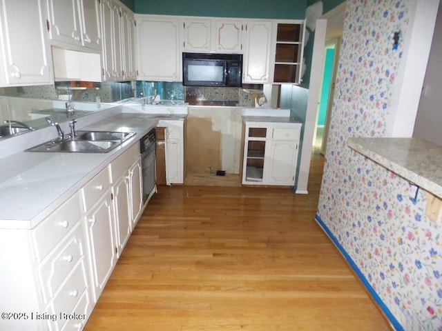 kitchen featuring tasteful backsplash, black appliances, light wood-style flooring, white cabinetry, and a sink