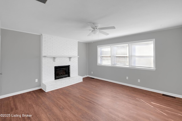 unfurnished living room with hardwood / wood-style flooring, ceiling fan, crown molding, and a brick fireplace