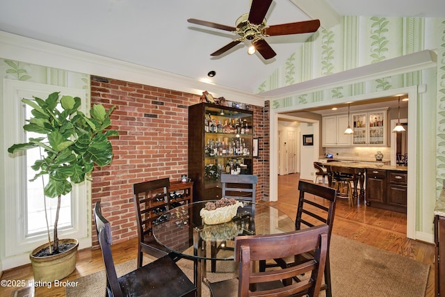 dining area with brick wall, hardwood / wood-style floors, and lofted ceiling