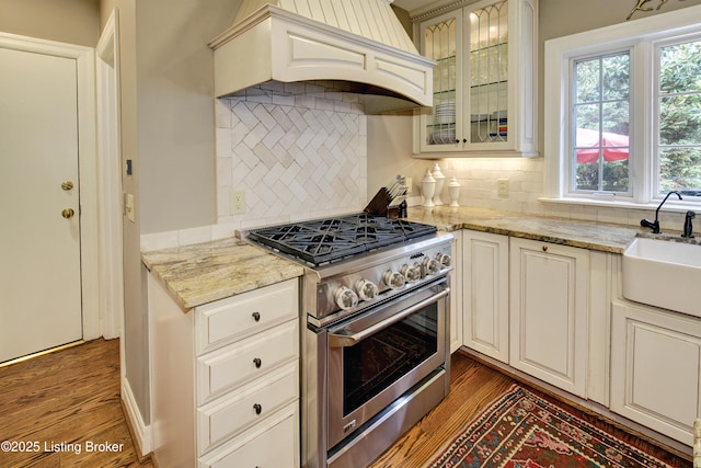 kitchen with sink, high end stainless steel range, light stone countertops, and custom range hood