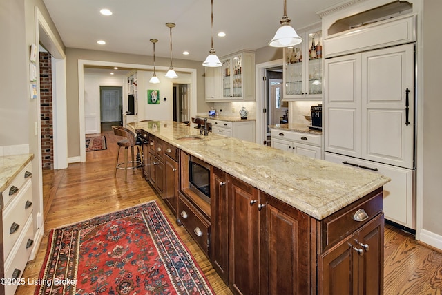 kitchen featuring stainless steel microwave, decorative light fixtures, sink, a kitchen island with sink, and dark brown cabinetry