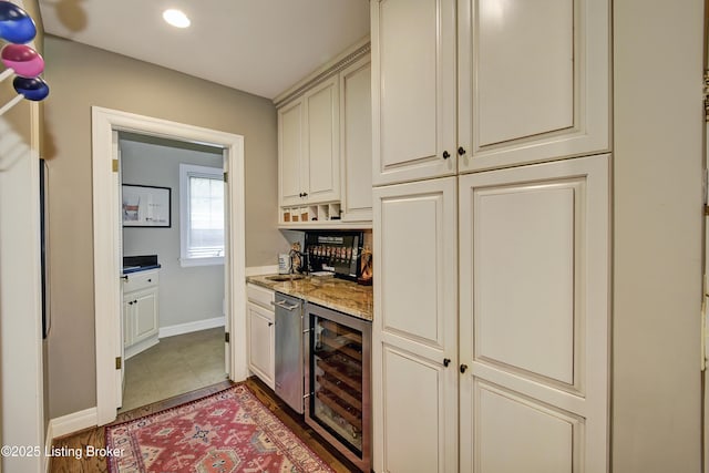 kitchen with sink, dark tile patterned floors, wine cooler, cream cabinets, and light stone countertops