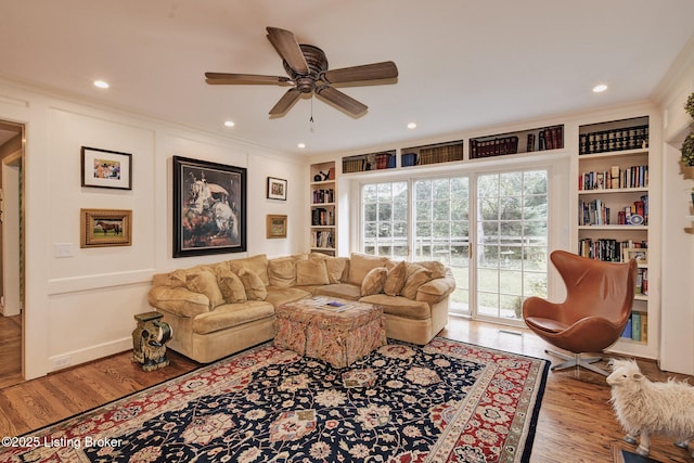 living room with crown molding, built in features, ceiling fan, and light wood-type flooring