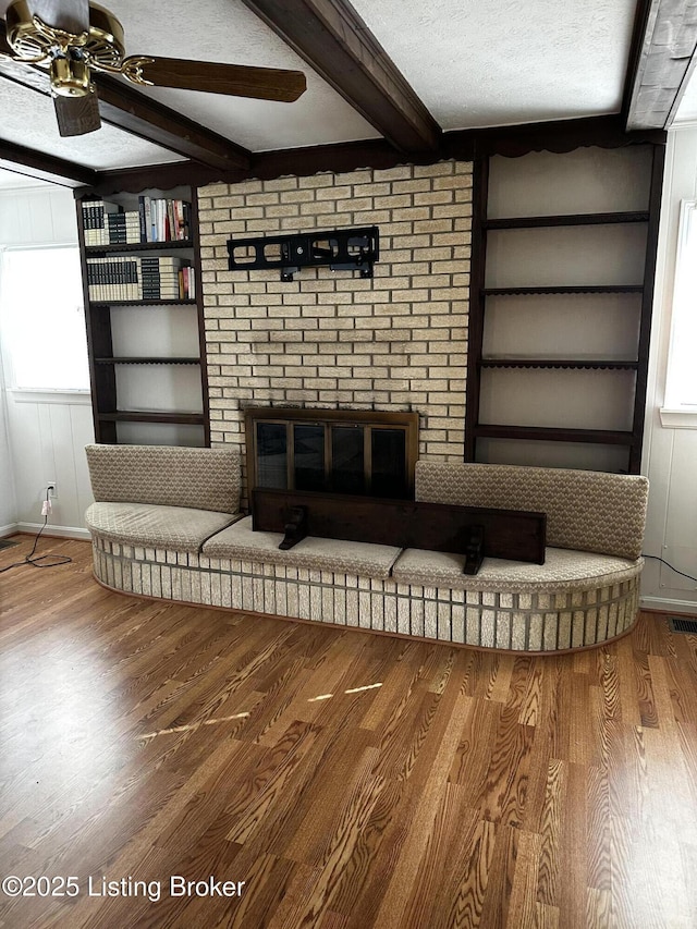 unfurnished living room with built in features, beamed ceiling, wood-type flooring, ceiling fan, and a textured ceiling