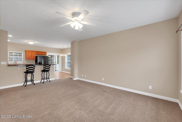 unfurnished living room with light carpet, sink, a textured ceiling, and ceiling fan