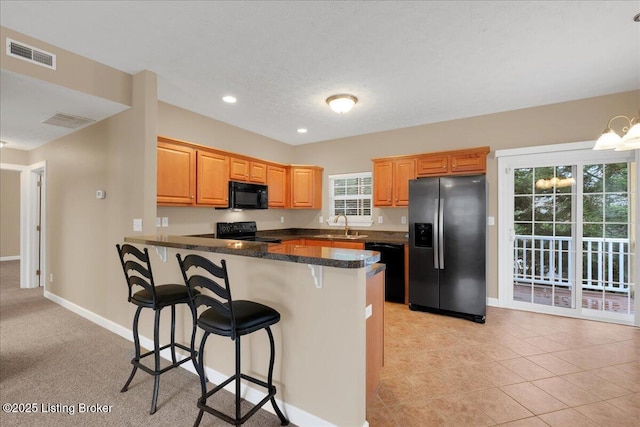 kitchen with sink, light tile patterned floors, a breakfast bar, black appliances, and kitchen peninsula