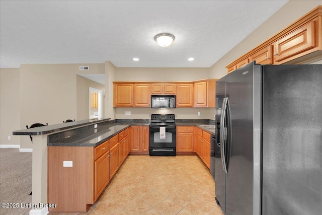 kitchen featuring black appliances, a breakfast bar area, dark stone counters, kitchen peninsula, and a textured ceiling