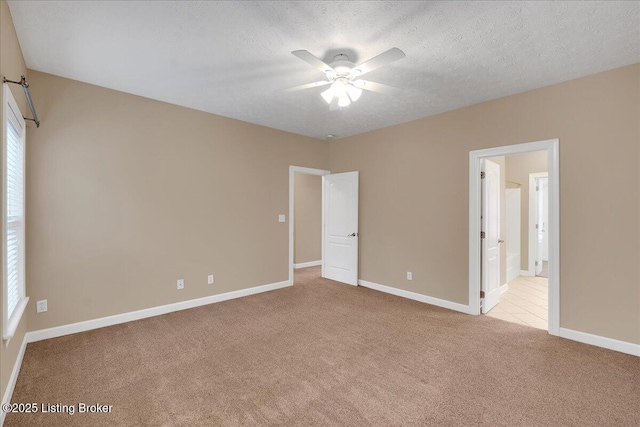 unfurnished bedroom with ceiling fan, light colored carpet, ensuite bath, and a textured ceiling