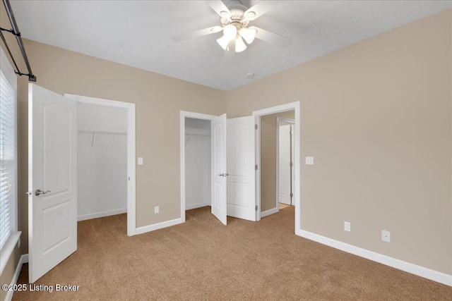 unfurnished bedroom with two closets, light carpet, and ceiling fan