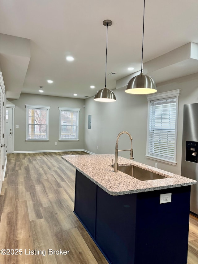 kitchen with hanging light fixtures, an island with sink, sink, and stainless steel fridge