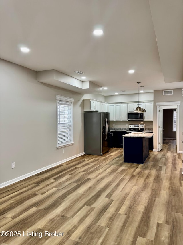 kitchen with light hardwood / wood-style flooring, appliances with stainless steel finishes, white cabinetry, an island with sink, and decorative light fixtures