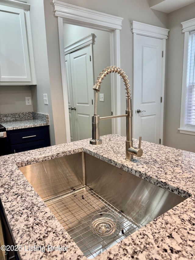 room details featuring white cabinetry, light stone countertops, and sink