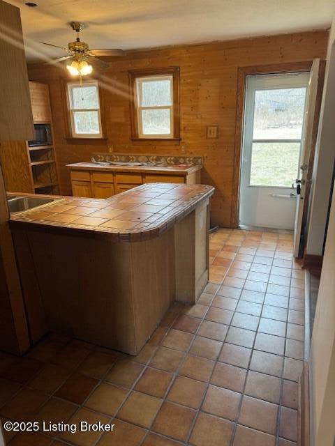 kitchen featuring wooden walls, tile counters, light tile patterned floors, ceiling fan, and kitchen peninsula