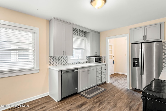 kitchen featuring gray cabinets, sink, decorative backsplash, stainless steel appliances, and dark wood-type flooring