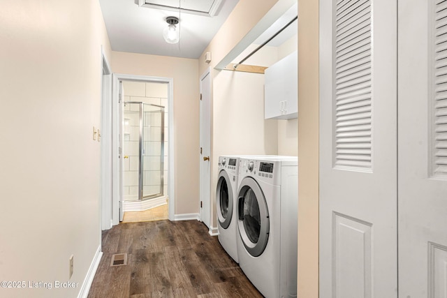 laundry area with dark wood-type flooring, washing machine and dryer, and cabinets