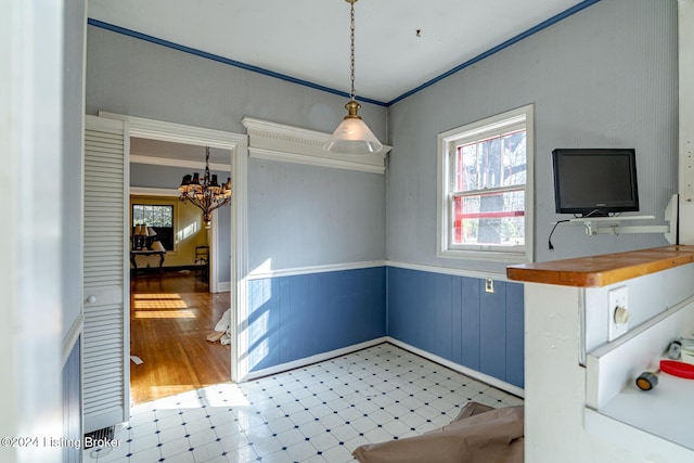 interior space with a chandelier, a wainscoted wall, crown molding, and light floors