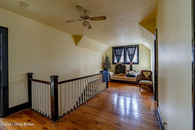 hall featuring lofted ceiling, light hardwood / wood-style flooring, and a textured ceiling