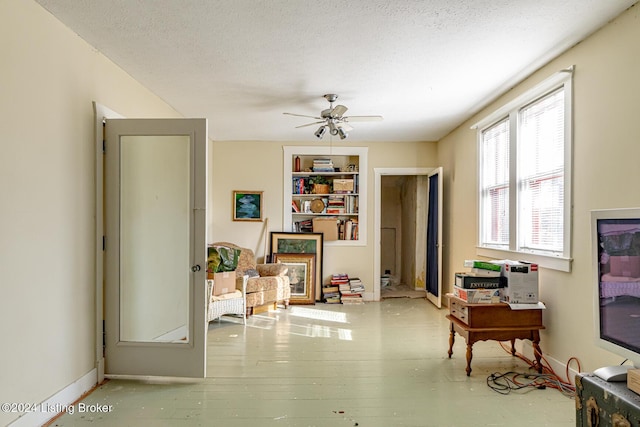 living area with ceiling fan, light wood-type flooring, built in features, and a textured ceiling