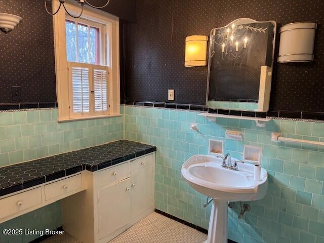 bathroom featuring wallpapered walls, tile walls, a wainscoted wall, tile patterned floors, and a sink