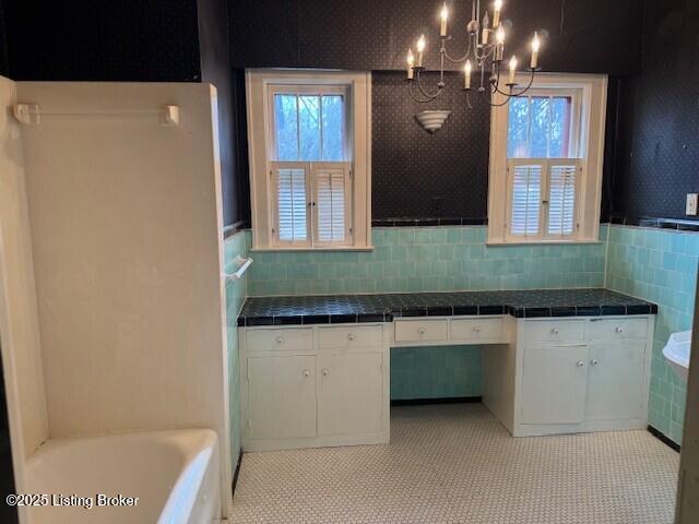 bathroom with tile walls, a washtub, a wealth of natural light, and a chandelier