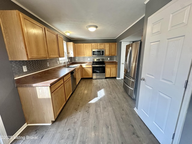 kitchen with sink, tasteful backsplash, crown molding, light hardwood / wood-style flooring, and stainless steel appliances