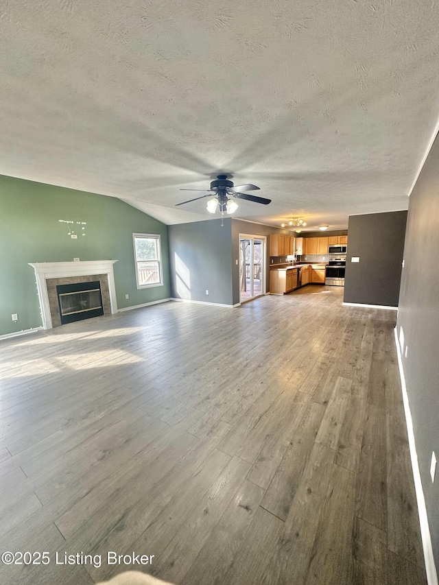 unfurnished living room with vaulted ceiling, ceiling fan, light hardwood / wood-style floors, and a textured ceiling