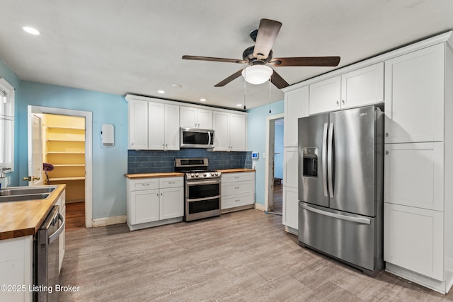 kitchen with stainless steel appliances, white cabinetry, sink, and wooden counters