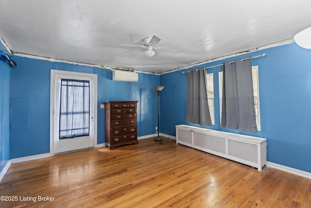 interior space with radiator, hardwood / wood-style flooring, an AC wall unit, and ceiling fan