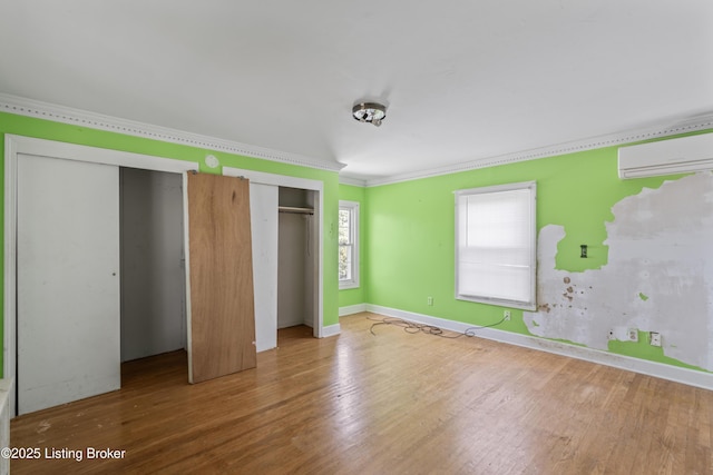 unfurnished bedroom with ornamental molding, a wall mounted AC, hardwood / wood-style floors, and two closets