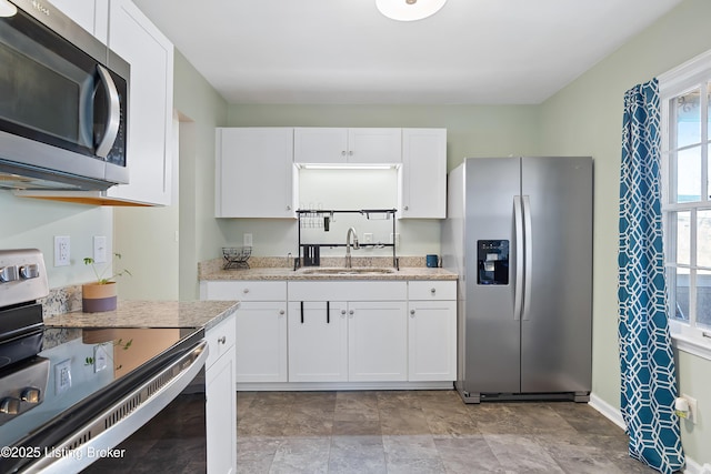 kitchen with stainless steel appliances, sink, white cabinets, and light stone counters