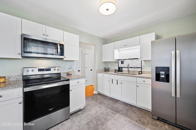 kitchen featuring stainless steel appliances, white cabinetry, light stone countertops, and sink