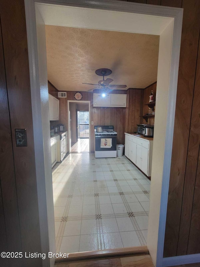 kitchen with gas range gas stove, ceiling fan, white cabinetry, wooden walls, and a textured ceiling