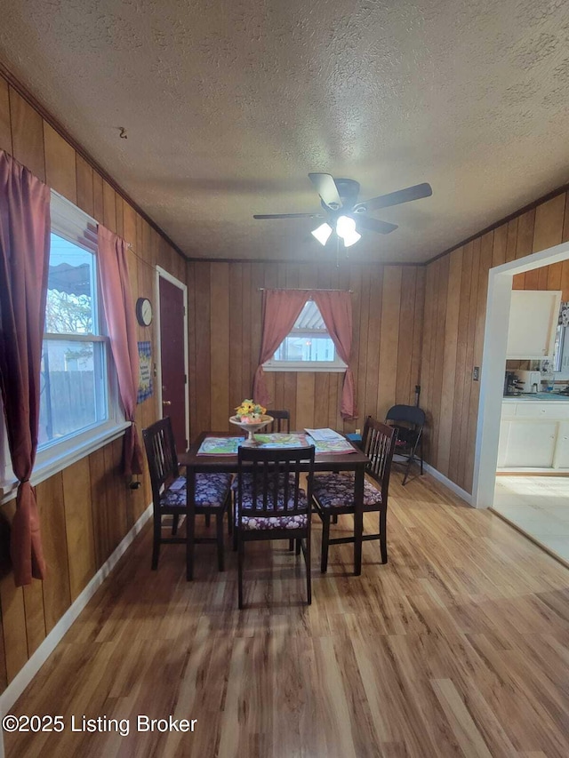 dining room featuring ceiling fan, wooden walls, a textured ceiling, and light wood-type flooring