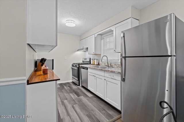 kitchen featuring sink, light hardwood / wood-style flooring, appliances with stainless steel finishes, a textured ceiling, and white cabinets