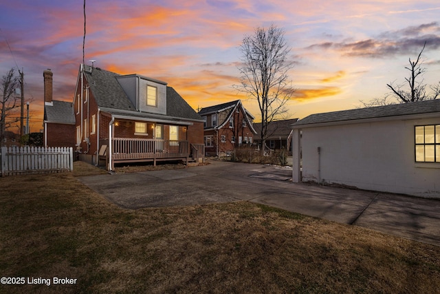 back house at dusk featuring a porch and a lawn