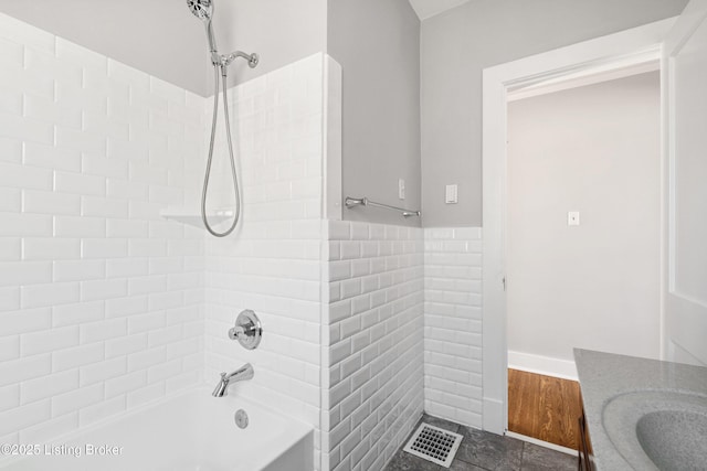 bathroom with tiled shower / bath combo, vanity, and tile walls