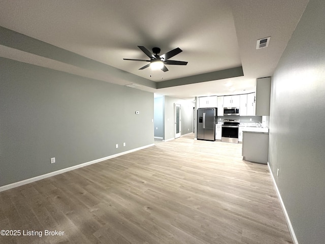 kitchen featuring white cabinetry, a tray ceiling, ceiling fan, stainless steel appliances, and light hardwood / wood-style floors