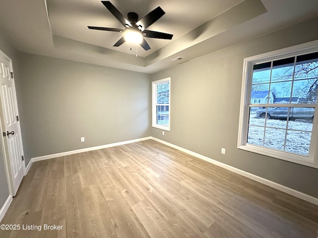 spare room with ceiling fan, a raised ceiling, and light hardwood / wood-style floors