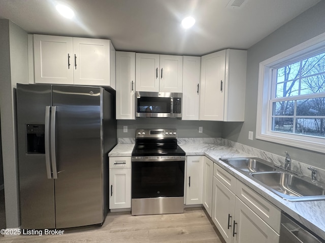 kitchen with appliances with stainless steel finishes, sink, white cabinets, and light hardwood / wood-style flooring