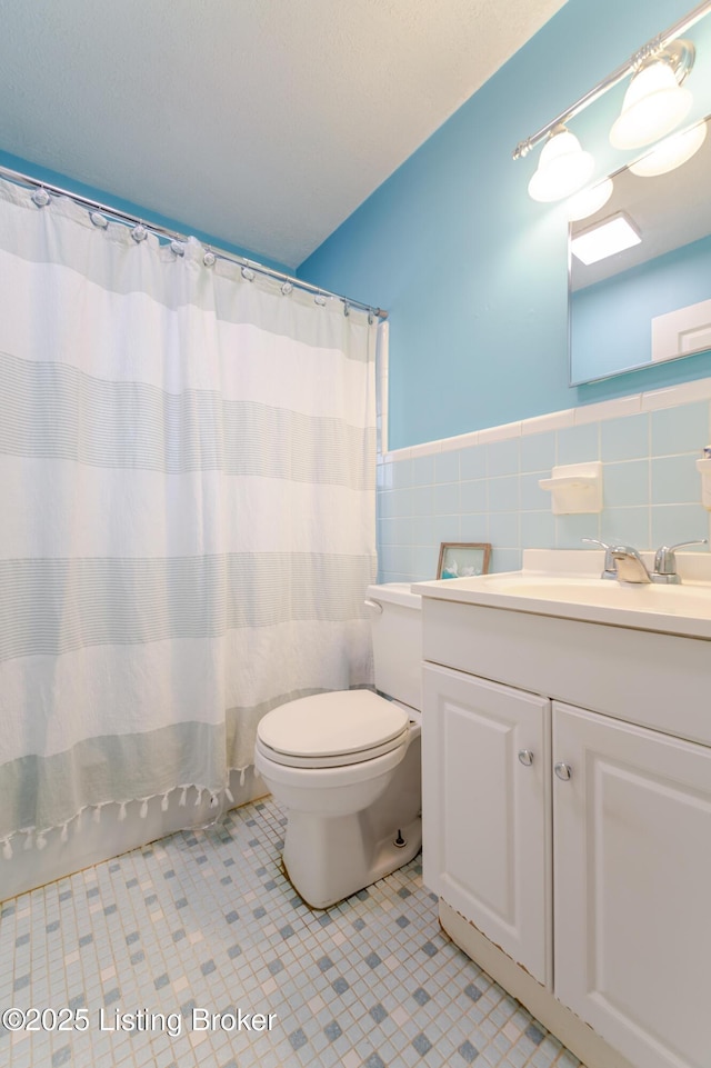 bathroom with curtained shower, tile walls, tile patterned flooring, vanity, and toilet