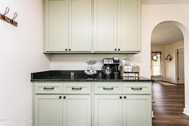 bar featuring dark stone countertops and dark hardwood / wood-style flooring