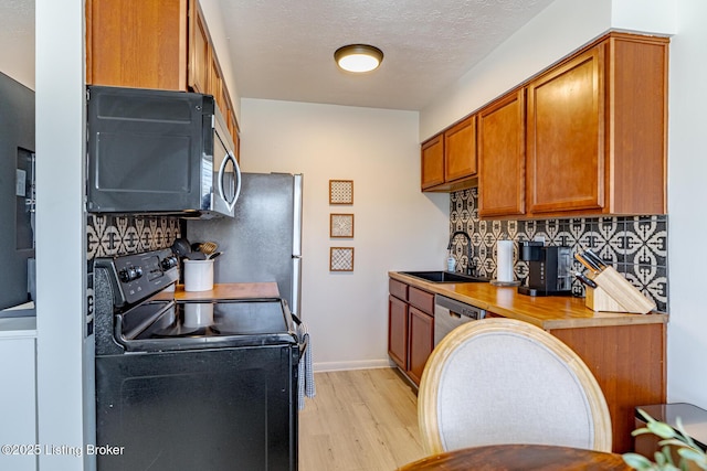 kitchen with stainless steel appliances, sink, decorative backsplash, and light wood-type flooring