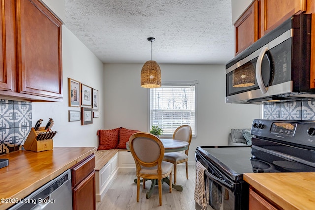 kitchen with appliances with stainless steel finishes, pendant lighting, tasteful backsplash, light wood-type flooring, and a textured ceiling